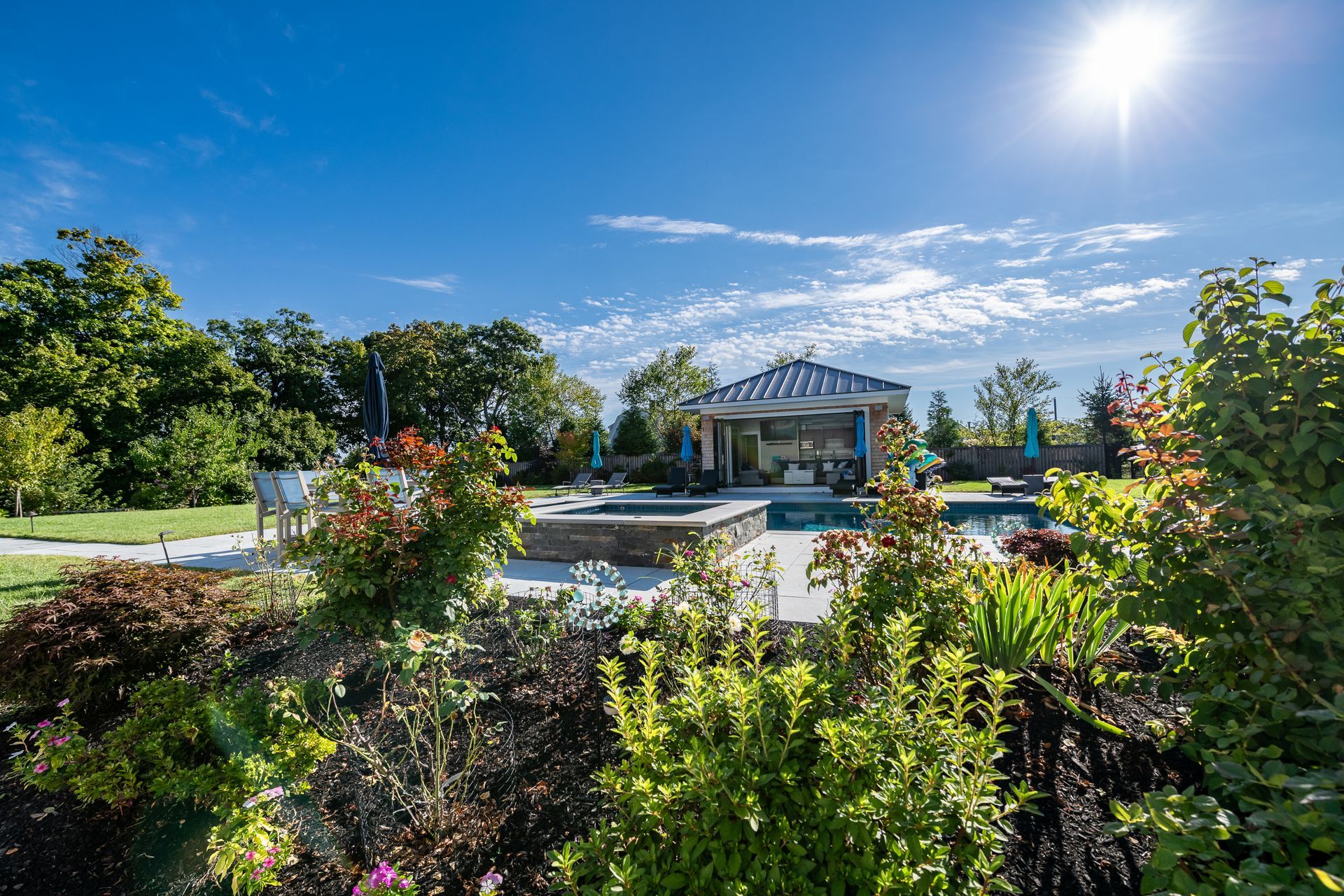 Sunny backyard with pool, gazebo, and lush landscaping under a blue sky.